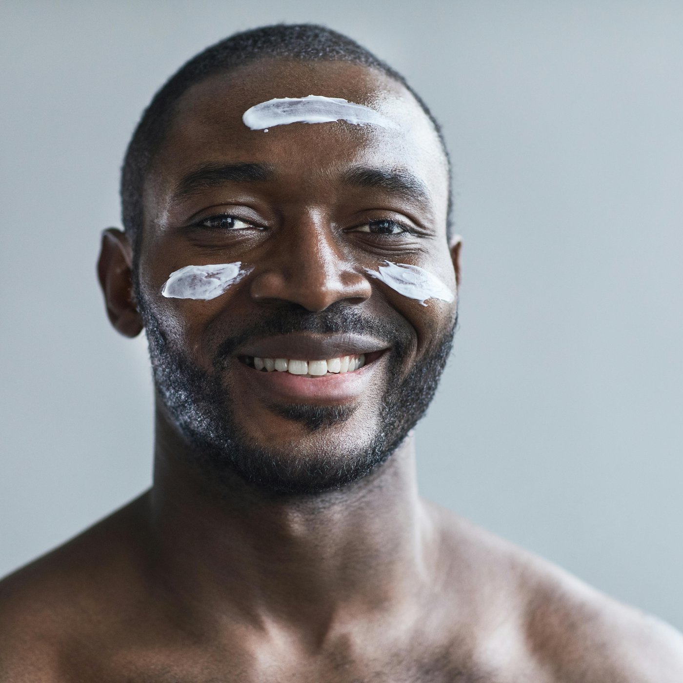 Smiling man with skincare cream applied to forehead and cheeks